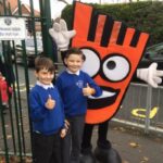 two pupils at the school gates with a mascot giving a thumb up sign