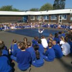 large group of pupils sitting in a square in the playground with an instructor on mats doing exercises