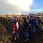 pupils with winter coats, hats and scarves looking at a rainbow