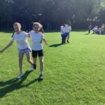 two pupils running in a sunny field wearing gym wear